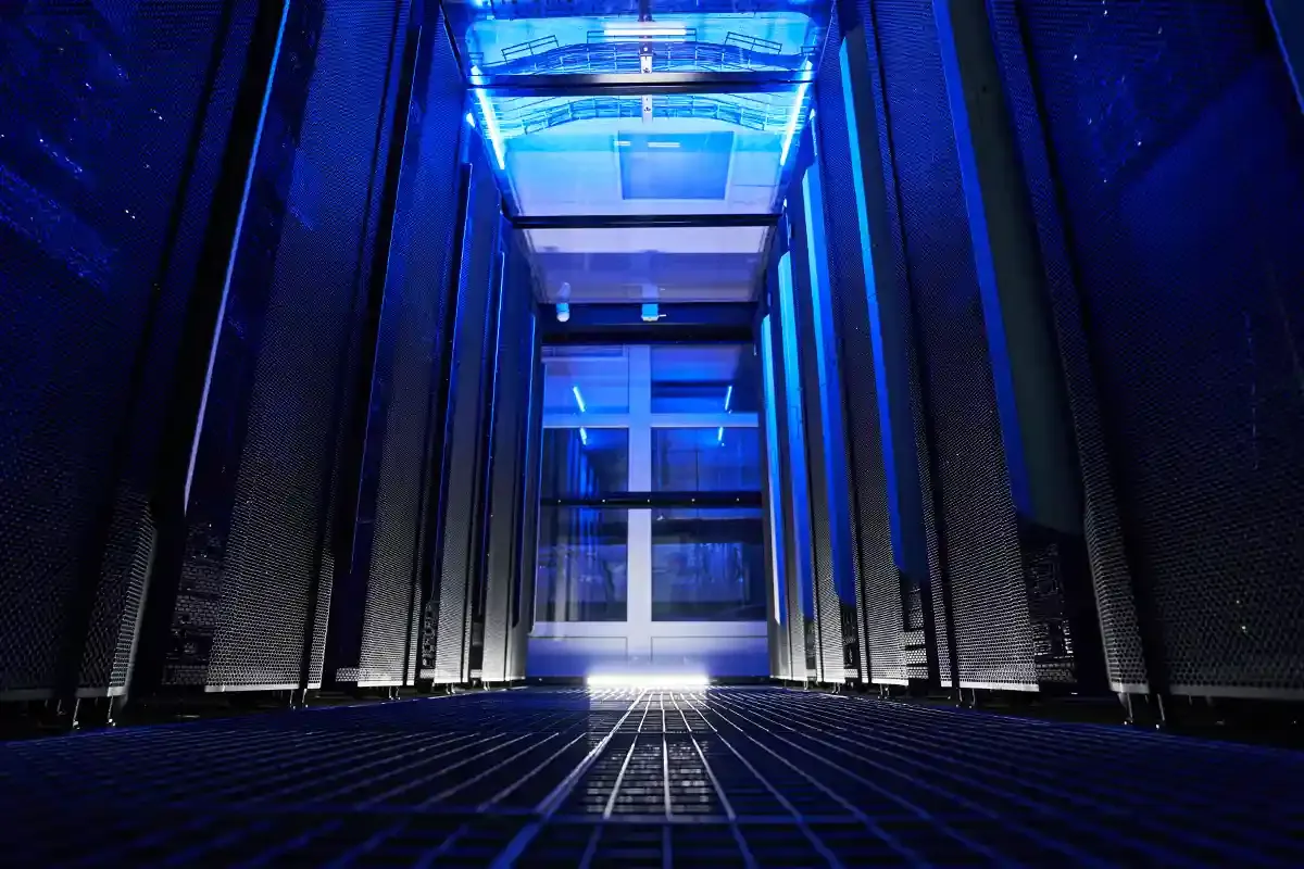 A row of server racks at night in a data centre, lit in a blue colour.
